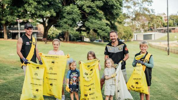 Clean Up Australia Day promo image of 2 males and 4 children in a park holding up yellow clean up bags
