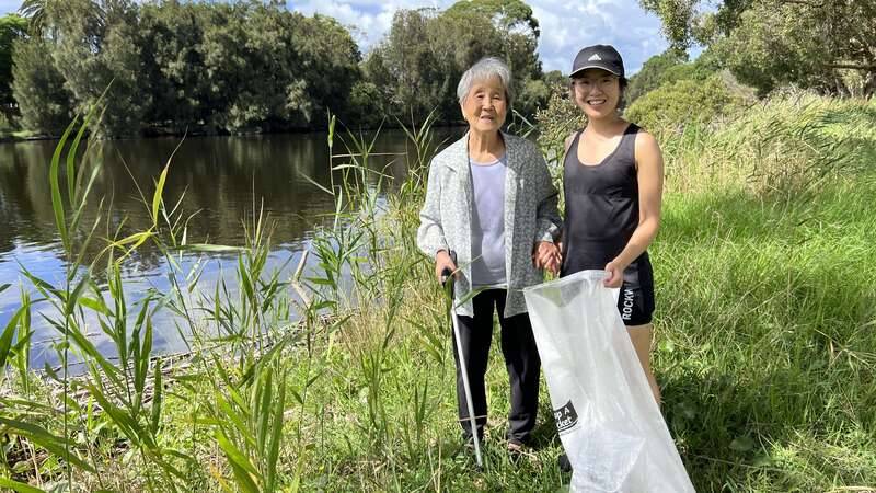 Older women and young woman walking in nature and picking up litter from next to the river