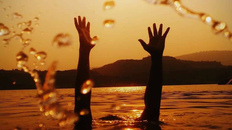 Person under water reaching hands up out of the water into the air, at sunset