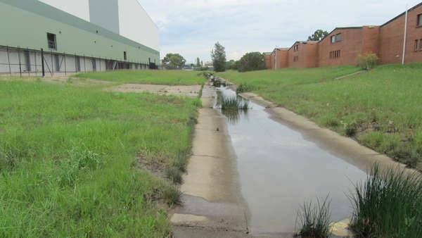 concrete stormwater canal with grass area each side running through a urban landscape