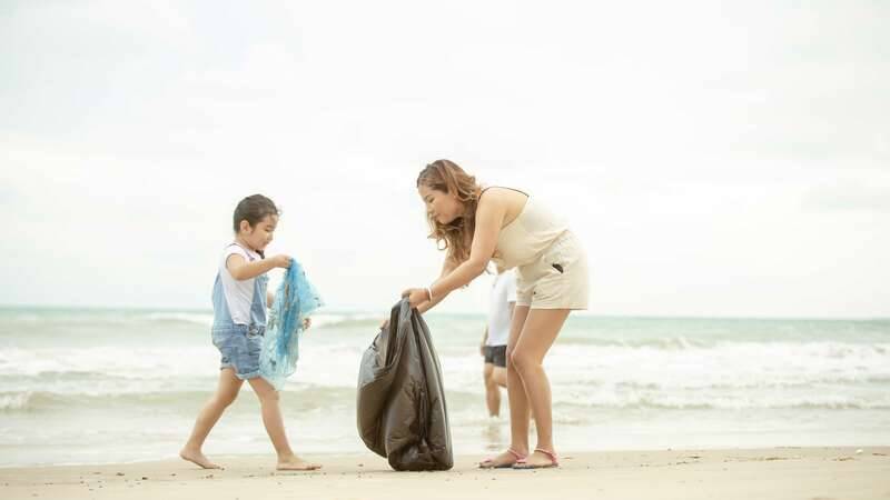 girl and woman picking up litter at the beach and putting it into a bin bag